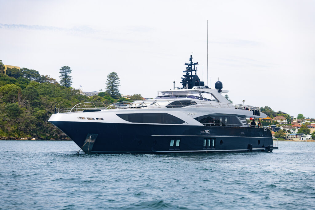Ghost II luxury superyacht anchored in Sydney Harbour, showcasing its sleek black and silver exterior design against a backdrop of lush greenery and waterfront homes.