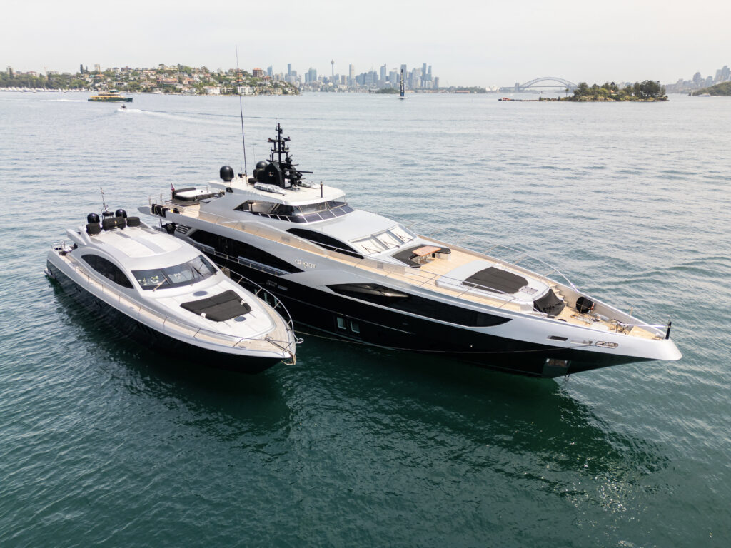 Aerial view of two black and silver luxury yachts anchored in Sydney Harbour with the cityscape and Harbour Bridge in the background.