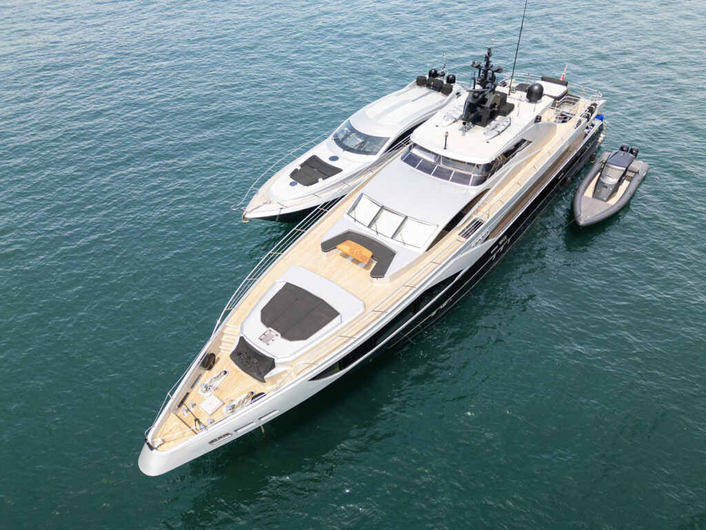 Aerial view of two modern luxury yachts and a black inflatable tender anchored on calm blue-green water.