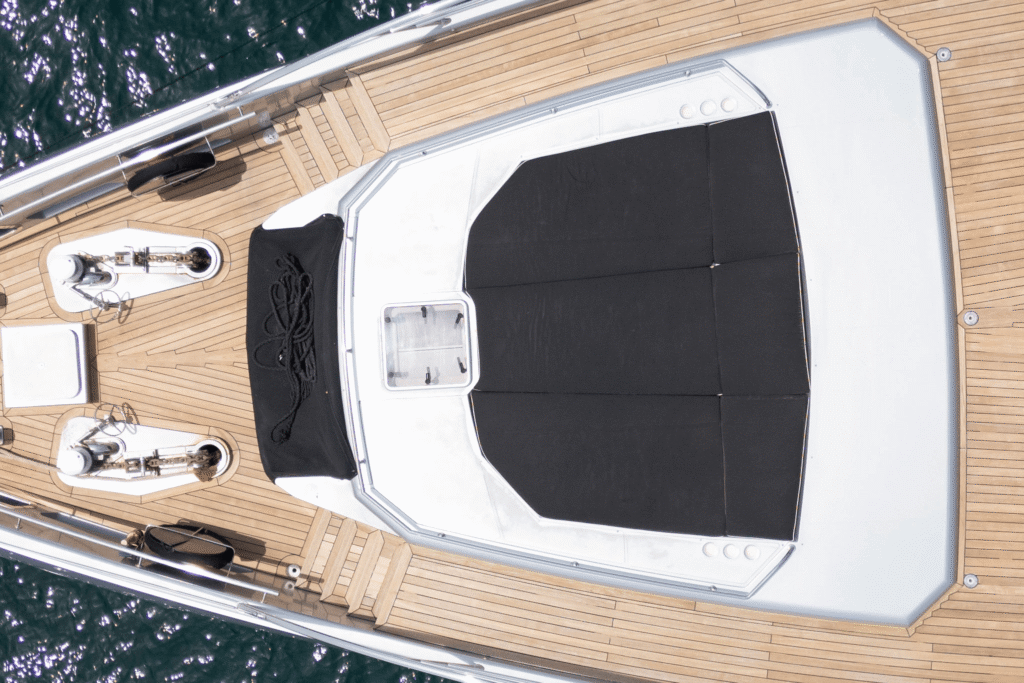 Aerial view of a luxury Ghost yacht’s bow deck featuring sun lounges, a wooden table, and sleek design details surrounded by deep blue ocean water.