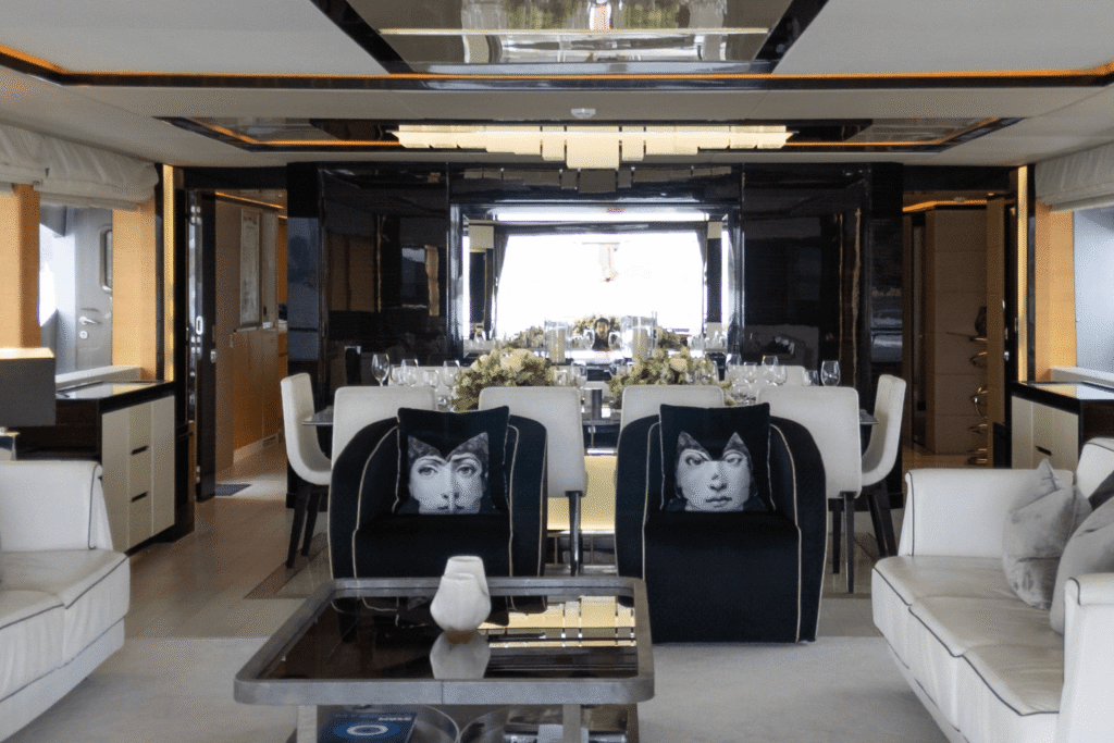 Luxurious dining and lounge area aboard the Ghost yacht, featuring modern decor with monochrome seating, artistic cushions, floral arrangements, and a sophisticated mirrored interior.