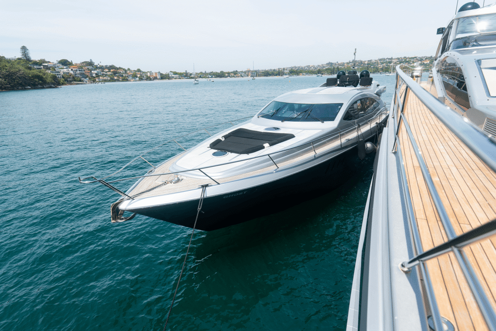 Luxury Ghost yacht anchored beside another vessel on the calm blue waters of Sydney Harbour, with waterfront homes visible in the background.